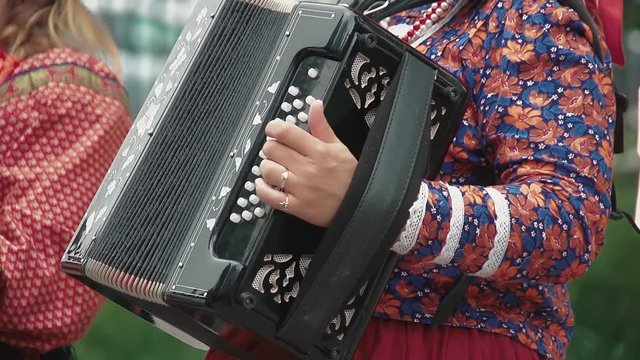 Women are dressed in folk costumes. One of them plays the accordion, the others dance and sing. Slow motion. Close up.