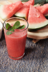 Glass of watermelon smoothie with some slice of the fruit on the background