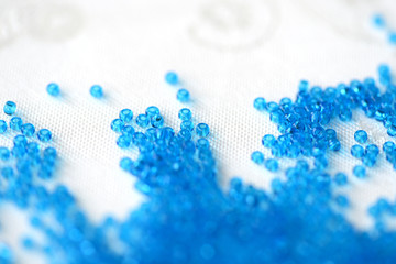 Transparent seed beads blue color scattered on a textile background close up