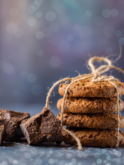 Chocolate cookies, stacked and tied with a rope, pieces of black chocolate, on a textured background. Vertical layout