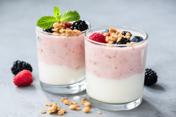 Yogurt with berries raspberry, blueberry and blackberry, crunchy granola and mint leaf in jar on concrete background. Closeup view. Healthy eating, healthy food and vegetarian vegan diet concept