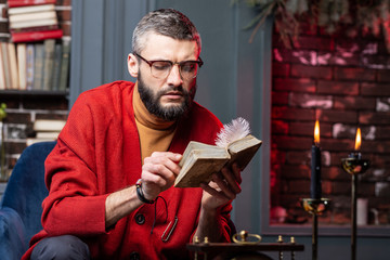 Bearded diviner sitting at the table with candles and enjoying self-education