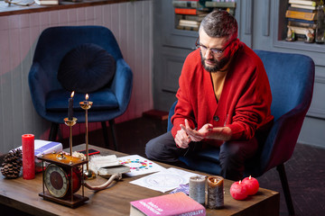 Bearded astrologist sitting in armchair reading book and doing practice