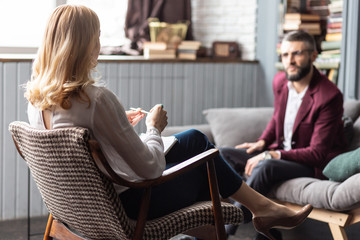 Blonde therapist wearing white blouse and dark trousers sitting near client