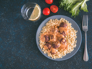 Bulgur dish idea and recipe. Bulgur with homemade roasted beef meatballs on dark blue background. Copy space for text. Top view or flat-lay.