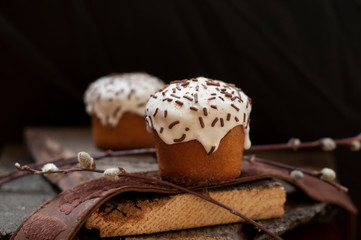 A  two small Easter cakes and a willow twig on a dark wooden background. Close up. Selective focus.