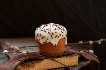 A   small Easter cake and a willow twig on a dark wooden background. Close up. Selective focus.