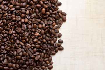 Black coffee grains lie on light wooden table, background image. place for text