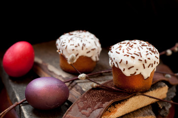A  two small Easter cake and dyed  eggs, and a willow twig on a dark wooden background. Close up. Selective focus.