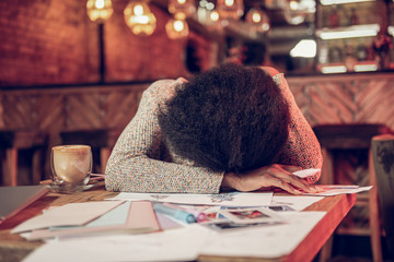 Disappointed afro-american female leaning on cafe table with fashion sketches