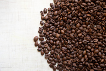 Black coffee grains lie on light wooden table, background image. place for text