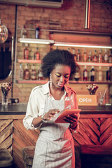 Pleasing alluring slim young African-American waitress checking information on tablet