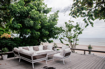 Tropical vacation wooden balcony with white fabric sofa couch under lush green tree.