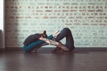 two beautiful caucasian women doing partner yoga in yoga studio opposite brick wall