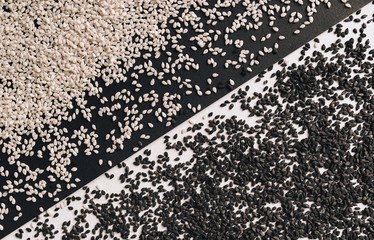 Black and white sesame seeds lie on opposite sides of a black and white background. The concept of calcium and iron, contrast and separation. Diagonal.