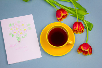 beautiful tulips ,cup of drink and handmade card with kid's drawing  for Mother's Day on blue background, top view