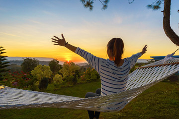 Asia woman sitting in hammock and hand up at mornig time, Selective focus.