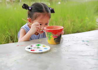 Intend Asian kid girl paint on earthenware dish. 