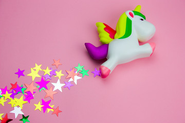 top view squishy toy  unicorn and glitters in the shape of stars on pastel pink background