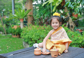 Asian child girl in traditional thai dress play making Thai culture dessert in the public garden. 