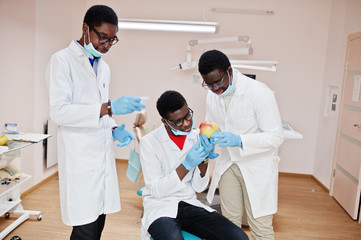 Fototapeta premium Three african american male doctors colleagues in dental clinic with an apple.