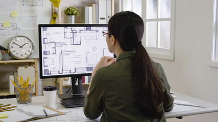 asian woman interior designer looking floor plan of new house indoor design on monitor concentrated...