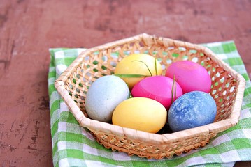 Multi-colored Easter eggs in a wicker basket on a brown background. Selective focus. Happy Easter concept.