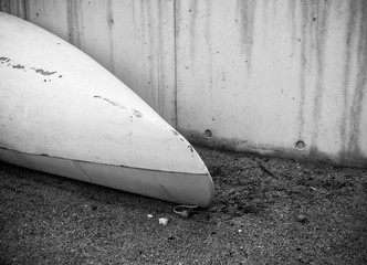 Kayak from white fiberglass plastic with aged marks with white cord on the beach with black sand with stones on seaside near concrete wall with no people, background with copyspace - image
