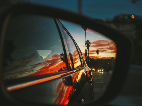 Beautiful bright red sunrise / sunset with palm trees and the city of Los Angeles is reflected in the side mirror of the car