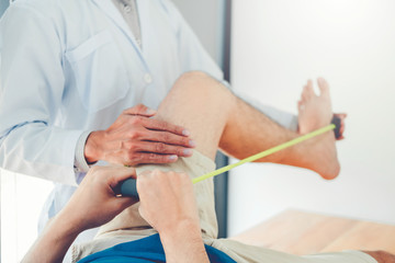 Fototapeta premium Physiotherapist man giving resistance band exercise treatment About knee of athlete male patient Physical therapy concept