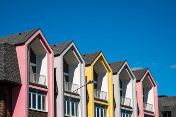 Rows of triangular elements of roofline covered with shingle against blue sky. Colorful pink and yellow house. Copy space