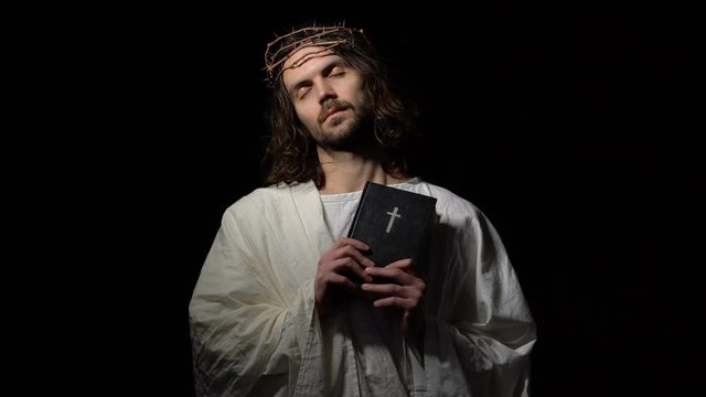 Jesus Christ with closed eyes in crown of thorns holding bible, spirit of god