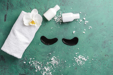 Under-eye patches with cosmetic products and towel on color background