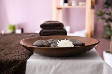 Plate with massage stones and flower on table in spa salon
