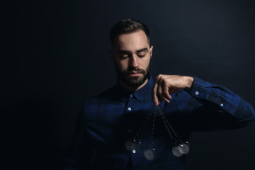 Male hypnotist with swinging pendulum on dark background
