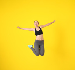 Young sporty woman jumping against color background