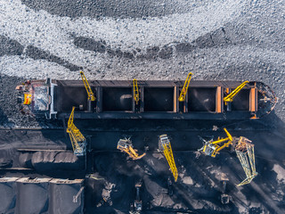 Loading coal mining in port on cargo tanker ship with crane bucket of train. Aerial top view