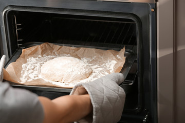 Putting of baking sheet with raw dough for bread into oven in kitchen