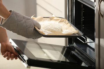 Putting of baking sheet with raw dough for bread into oven in kitchen