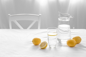 Jug and glass with fresh water and lemons on table