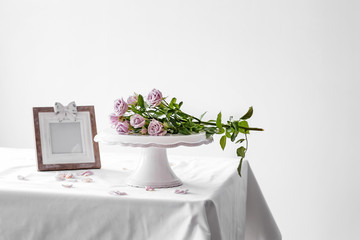 Dessert stand with fresh rose flowers on table against light background