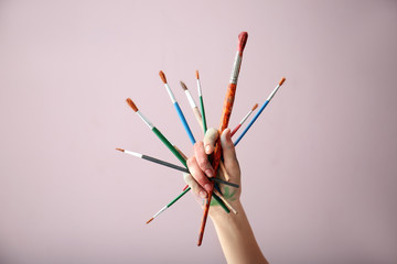 Painted female hand with brushes on color background