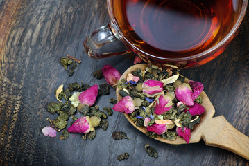 a cup of tea. green tea with flowers in a wooden spoon on a dark wooden table. green tea with flowers and dry fruit pieces. blend tea. top view