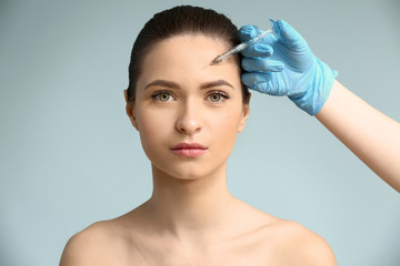 Young woman receiving injection in face on color background