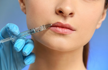 Young woman receiving injection in face on color background, closeup