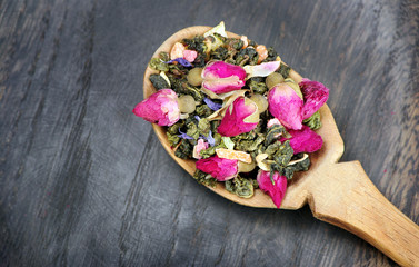 green tea with flowers in a wooden spoon on a dark wooden table. green tea with flowers and dry fruit pieces. blend tea. top view.