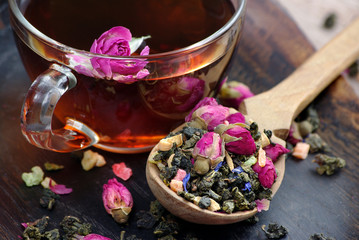 a cup of tea. green tea with flowers in a wooden spoon on a dark wooden table. green tea with flowers and dry fruit pieces. blend tea. close up