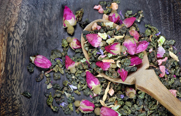 green tea with flowers in a wooden spoon on a dark wooden table. green tea with flowers and dry fruit pieces. blend tea. 