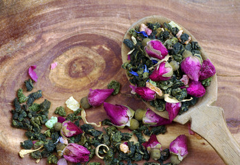 green tea with flowers in a wooden spoon on a wooden table. green tea with flowers and dry fruit pieces. blend tea. top view.