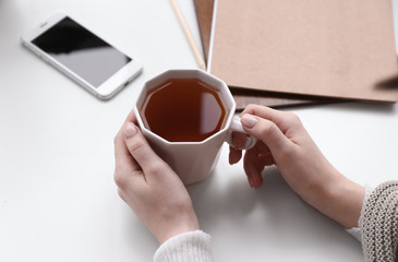 Woman with cup of hot tea on white table, closeup